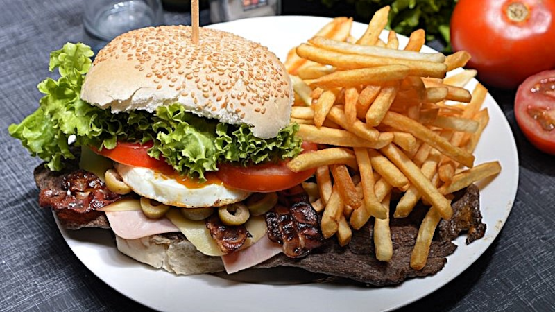 Fettiger Burger mit und Speck sowie Pommes auf einem Teller
