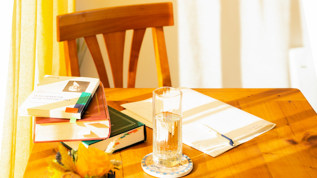 Tisch mit Trinkwasser in einem Glas und Notizblock sowie diverse Fachbücher